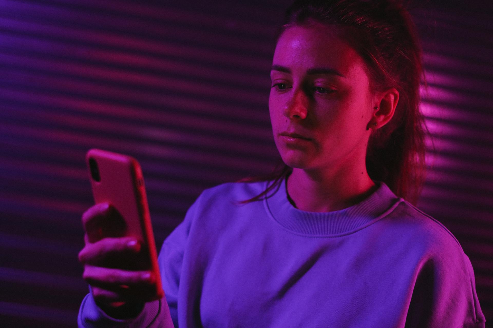 A woman using her phone in a dark room with colorful lights | Source: Pexels