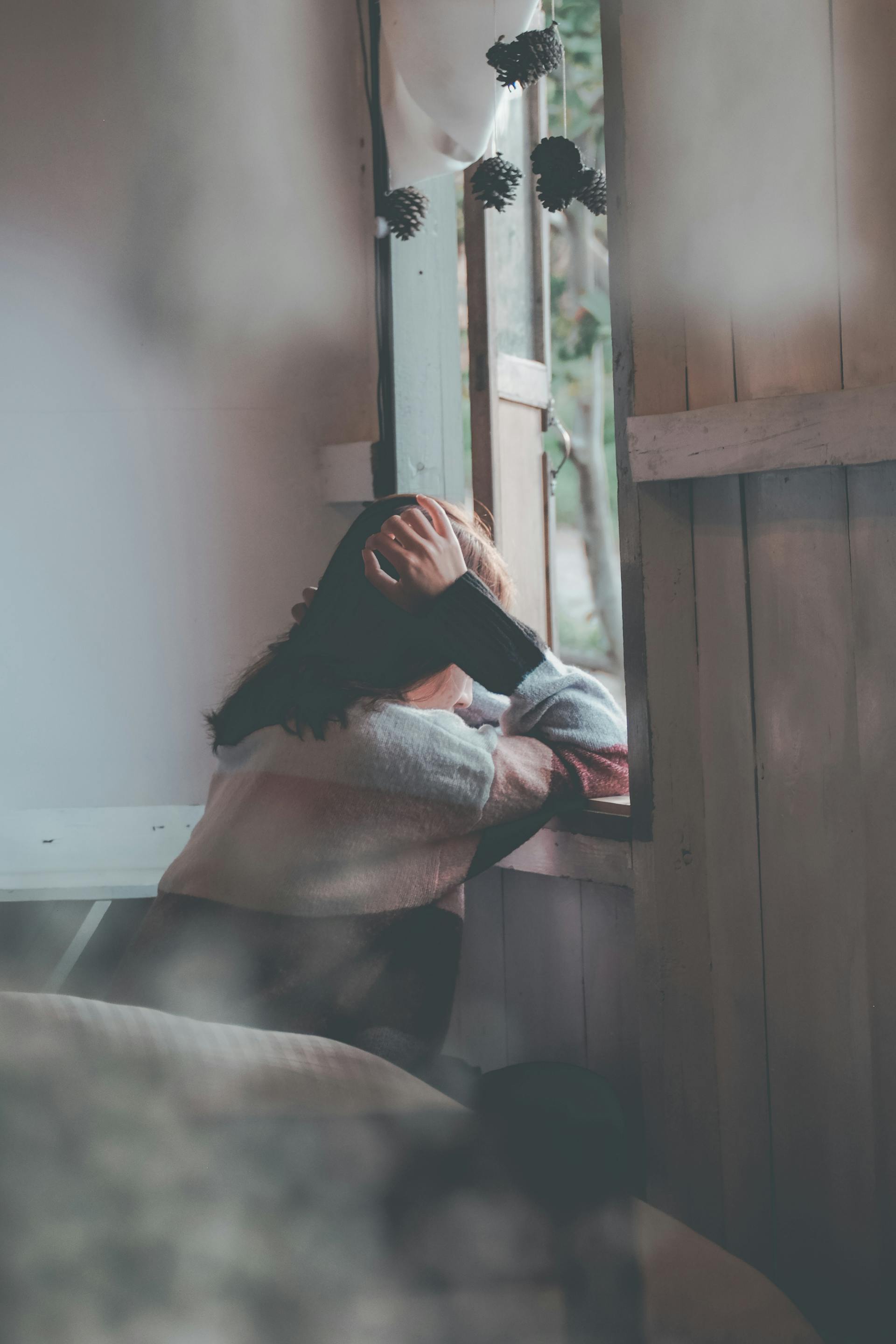 A back-view shot of a sad woman leaning on a wooden window | Source: Pexels